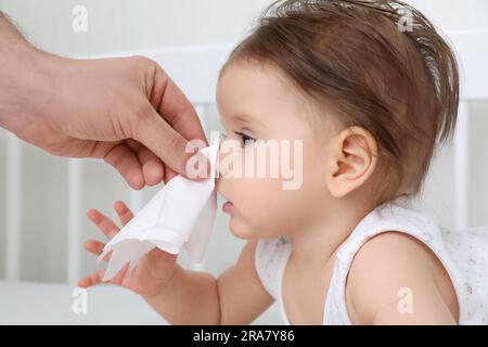 Père essuyant le nez liquide du petit bébé avec une serviette sur le lit, gros plan Banque D'Images