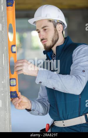 workman tenant le niveau à bulle verticalement contre le mur Banque D'Images