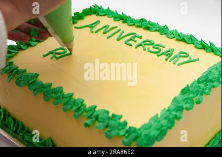 Femme écrivant avec un sac de pâtisserie sur un gâteau d'anniversaire vert et jaune isolé sur fond blanc. Banque D'Images