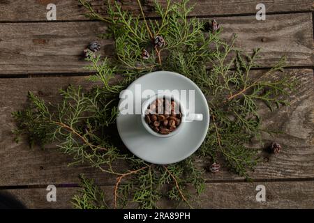 tasse blanche pleine de grains de café torréfiés sur des branches avec un arbre de noël sur la table, nouveau design de l'année Banque D'Images