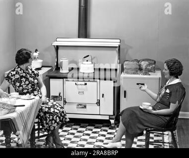 Beaver Dam, Wisconsin : 1937. Deux femmes s'assoient dans une cuisine buvant du café tandis que du pain fraîchement cuit refroidit sur le meuble Banque D'Images