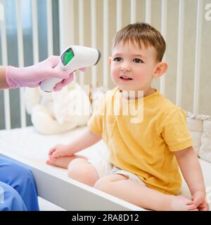 Le médecin utilise un thermomètre électronique pour mesurer la température de l'enfant assis sur le lit. Enfant âgé d'environ deux ans (un an onze Banque D'Images