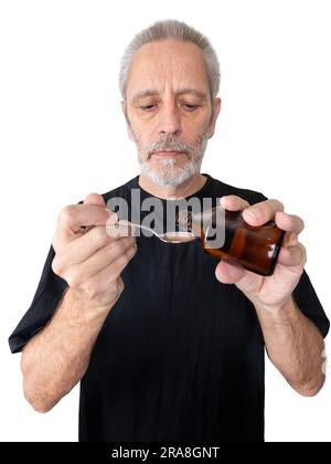 Un homme mûr verse du sirop de toux dans une cuillère pour guérir son mal de gorge et sa bronchite. Isolé sur blanc Banque D'Images