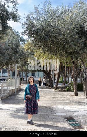 Portrait d'une jeune fille brune de vingt-cinq ans vêtue d'une robe bleue vintage avec un motif et un chemisier vert avec un petit sac à main Banque D'Images