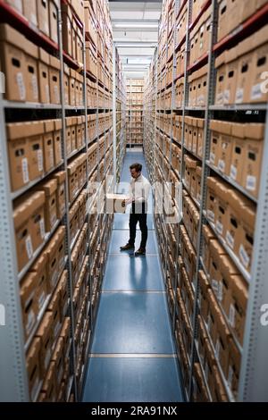 Laurence Ward, responsable des services numériques pour les Archives métropolitaines de Londres (LMA), retire une boîte de l'installation de stockage des plus grandes archives historiques du Royaume-Uni. Avec plus de 100km livres, cartes, photographies, films et documents datant de 1067 détenus dans des salles fortes, le LMA est le principal dépôt d'archives du gouvernement local pour la région du Grand Londres, y compris la City de Londres et est le plus grand bureau de disques du comté au Royaume-Uni. Date de la photo: Mardi 27 juin 2023. Banque D'Images