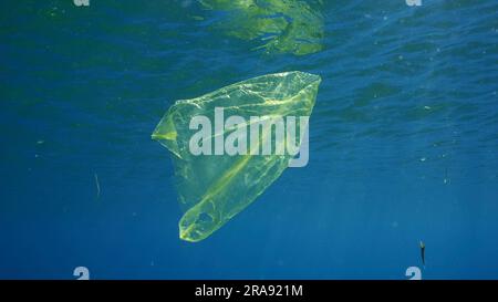 Le sac en plastique jetable jaune utilisé dérive sous la surface de l'eau bleue dans les rayons solaires. Déchets plastiques polluant les mers et les océans, Mer Rouge, Egypte Banque D'Images