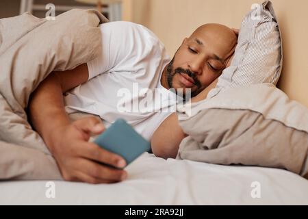 Portrait d'un homme noir adulte allongé au lit à la maison et à l'aide des réseaux sociaux défilants de smartphone Banque D'Images