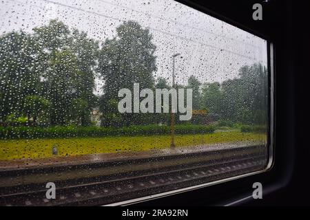 Vue depuis la fenêtre du train sur le temps pluvieux en été. La fenêtre du train est recouverte de gouttes de pluie. Banque D'Images