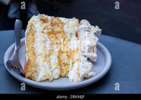 Une seule portion plaquée d'un gâteau de meringue au citron fait maison servi à une table plaquée. le gâteau a une garniture au citron caillé et un glaçage à la crème au beurre Banque D'Images