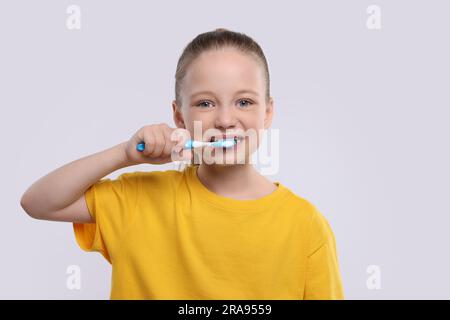 Bonne fille se brossant les dents avec une brosse à dents sur fond blanc Banque D'Images
