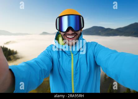 Jeune homme souriant dans des lunettes de ski prenant le selfie dans les montagnes Banque D'Images