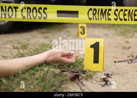 Scène de crime avec le corps de la femme morte, marqueur, couteau sanglant et ruban jaune dehors, gros plan Banque D'Images