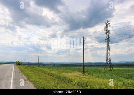 Tours de transmission de puissance au-dessus d'un champ rural dans la campagne. Ciel sombre avec des nuages. Banque D'Images