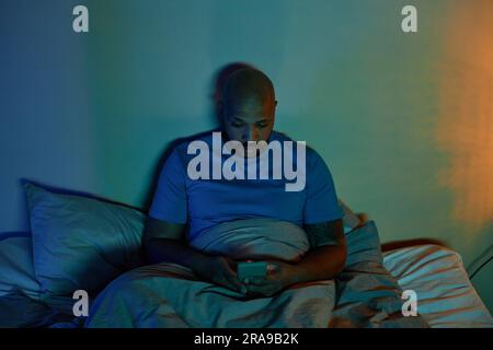 Portrait d'un homme adulte noir utilisant un smartphone au lit la nuit souffrant d'insomnie Banque D'Images