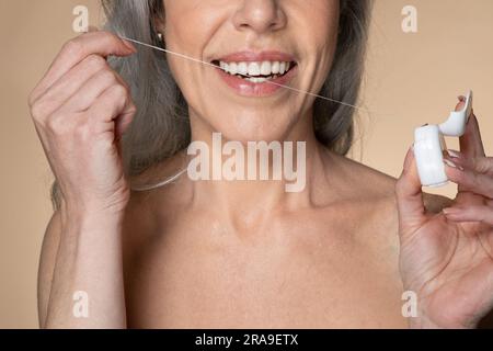 Soins de la bouche et traitement de la bouche. Gros plan coupe courte d'une femme sénior méconnue à cheveux gris utilisant une soie dentaire Banque D'Images