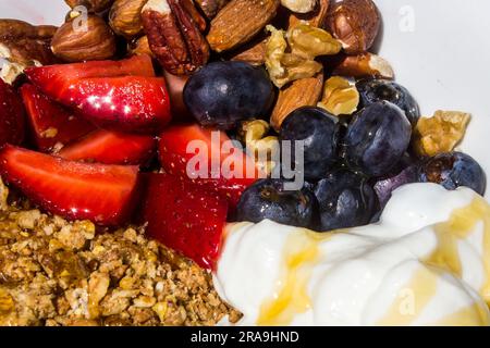 Gros plan de fraises fraîches coupées, de noix, de bleuets et de yaourts, tous assaisonnés de miel Banque D'Images