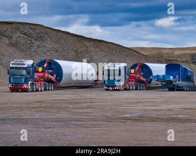 Les camions attendent de prendre des sections de tour de soutien d'éolienne à leurs sites de construction. Des travaux sont en cours pour construire le parc éolien Viking à Shetland, au Royaume-Uni. Banque D'Images