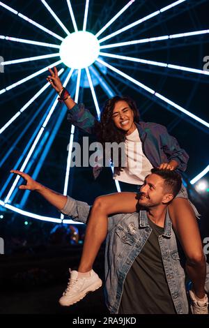 Couple heureux de s'amuser la nuit contre les lumières de la roue de ferris Banque D'Images