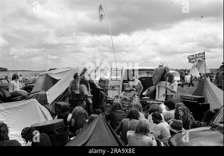 Les hippies se produisent lors d'un concert de rock improvisé parmi leurs tentes. Une petite foule se réunit pour écouter. Festival libre de Stonehenge au solstice d'été, Wiltshire, Angleterre juin 1976. ANNÉES 1970 ROYAUME-UNI HOMER SYKES Banque D'Images