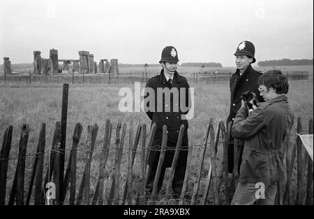 Festival libre de Stonehenge au solstice d'été, Wiltshire, Angleterre juin 1976. Le cercle de pierre hors limites, deux policiers parlent à un festivalier qui tient son chat de compagnie. ANNÉES 1970 ROYAUME-UNI HOMER SYKES Banque D'Images