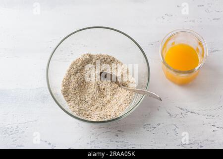 Un bol en verre avec flocons d'avoine moulus et un verre de jus d'orange fraîchement pressé sur fond gris clair, vue du dessus. Cuisiner un petit-déjeuner maison sain Banque D'Images