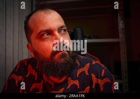 Portrait d'un homme adulte avec une barbe, travaille devant un ordinateur, lumière de couleur mixte, intérieur Banque D'Images