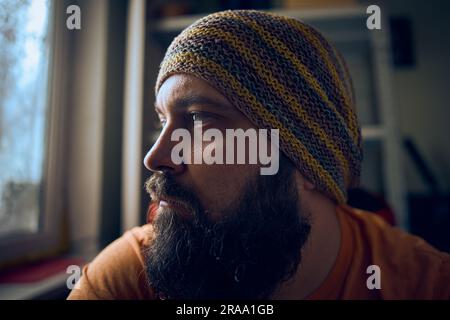 Un homme avec une barbe portant un chapeau rayé et un t-shirt, regardant vers le haut dans la fenêtre Banque D'Images