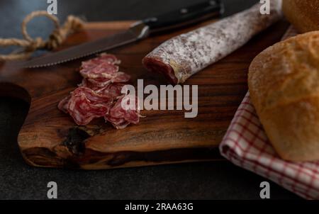 Tranché de salami espagnol, fuetec de porc iberico sur une planche de bois avec couteau Banque D'Images