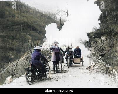 Un pilote d'expédition britannique sur une moto est tenu par une sentinelle à une barricade de fils barbelés en raison de l'explosion d'une carapace de gaz à proximité. Un officier dans une voiture de côté monte la route et tous portent des masques à gaz sur le front occidental en France pendant la première Guerre mondiale en 1918 Date: 1918 Banque D'Images