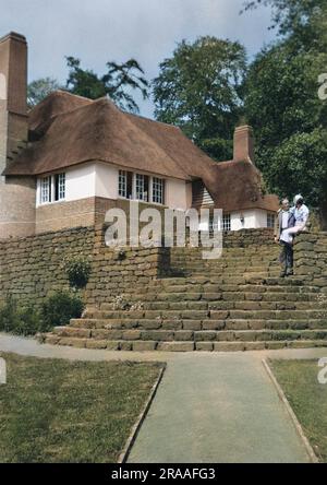 Un couple dans un jardin bien entretenu à l'arrière d'un grand cottage en chaume. Banque D'Images