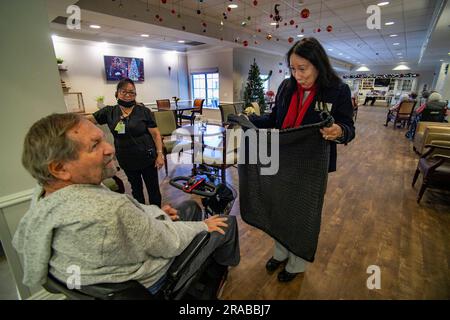 Un membre bénévole hispanique d'un groupe de tricotage catholique distribue son travail à une maison de soins pour personnes âgées en fauteuil roulant résidant à San Ju Banque D'Images