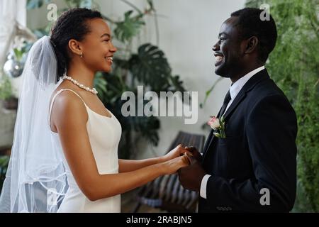 Vue latérale portrait de jeune couple noir en tant que mariée et marié regardant les uns les autres et tenant les mains Banque D'Images