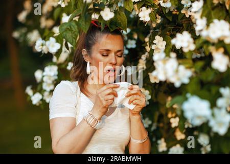 Heure d'été. triste femme élégante en chemise blanche avec mouchoir a une attaque d'allergie près de l'arbre de floraison. Banque D'Images