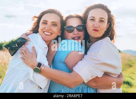 Portrait de trois femmes souriantes et souriantes qui embrassent pendant la marche en plein air. Ils regardent la caméra. Femme amitié, relations, et bonheur conc Banque D'Images