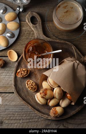 Petits gâteaux faits maison en noyer fraîchement cuits, lait concentré cuit, plat de cuisson et une tasse de café sur une table en bois, plat Banque D'Images