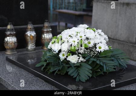 Couronne funéraire de fleurs et lanternes sur pierre tombale de granit dans le cimetière Banque D'Images