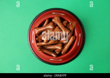 Bol rouge avec biscuits en forme d'os pour chiens sur fond vert, vue du dessus Banque D'Images