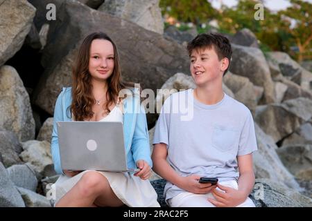 les adolescents communiquent dans la nature garçon et fille avec des gadgets portable téléphone timide regarder dans les yeux première date relation. L'amour à l'adolescence être distrait d'Internet être dans la vraie vie sourire lumineux Européens Banque D'Images