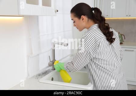 Femme dans des gants en caoutchouc utilisant le détachant de moule sur le plan de travail dans la cuisine Banque D'Images