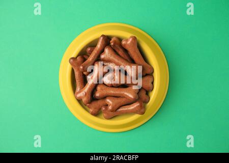 Bol jaune avec biscuits en forme d'os pour chiens sur fond vert, vue du dessus Banque D'Images