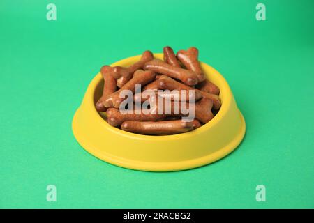 Bol jaune avec biscuits en forme d'os pour chiens sur fond vert Banque D'Images