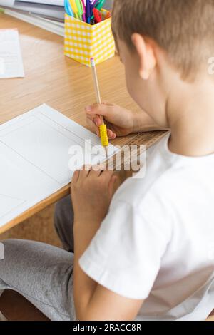 Un joli garçon fait un dessin avec une règle et un crayon. Leçons à la maison. Géométrie et dessin. Banque D'Images