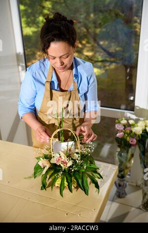 Vue en hauteur d'une fleuriste féminine créant un arrangement de fleurs avec des fleurs d'orchidées fraîches et des plantes, en insérant une carte d'anniversaire pour spécial Li festif Banque D'Images