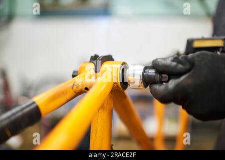 Entretien d'un vélo : mains d'une personne méconnaissable utilisant des gants pour démonter un vélo orange dans son atelier de réparation. Banque D'Images