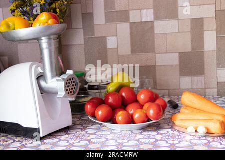 moulin à viande électrique au poivre sur la table à côté des tomates et des carottes sur la table dans la cuisine, la cuisine adijika maison, préparatio maison Banque D'Images