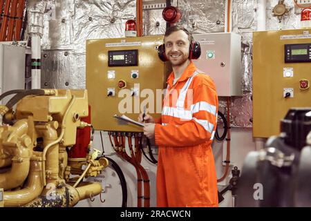 Jeune ingénieur professionnel offshore vérifiant les paramètres du moteur de travail dans la salle des machines. Ingénieur offshore effectuant des contrôles sur les machines en marche. Banque D'Images