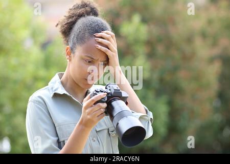Photographe noir se plaignant de vérifier des photos sur l'appareil photo dans un parc Banque D'Images
