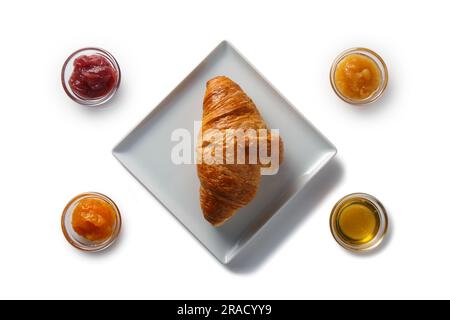 Croissant sur une soucoupe carrée et divers types de confiture et de miel dans des bols. Isolé sur fond blanc. Banque D'Images