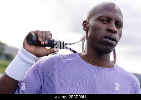 Portrait d'un joueur de tennis afro-américain sérieux tenant une raquette de tennis sur un court extérieur Banque D'Images