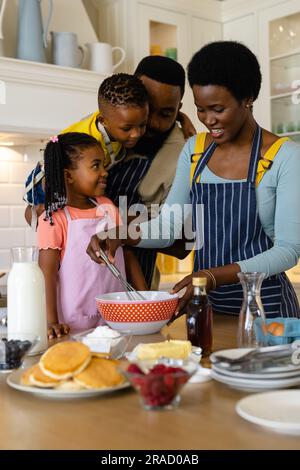 Père afro-américain avec fils et fille regardant la mère mélanger la pâte dans un bol dans la cuisine Banque D'Images